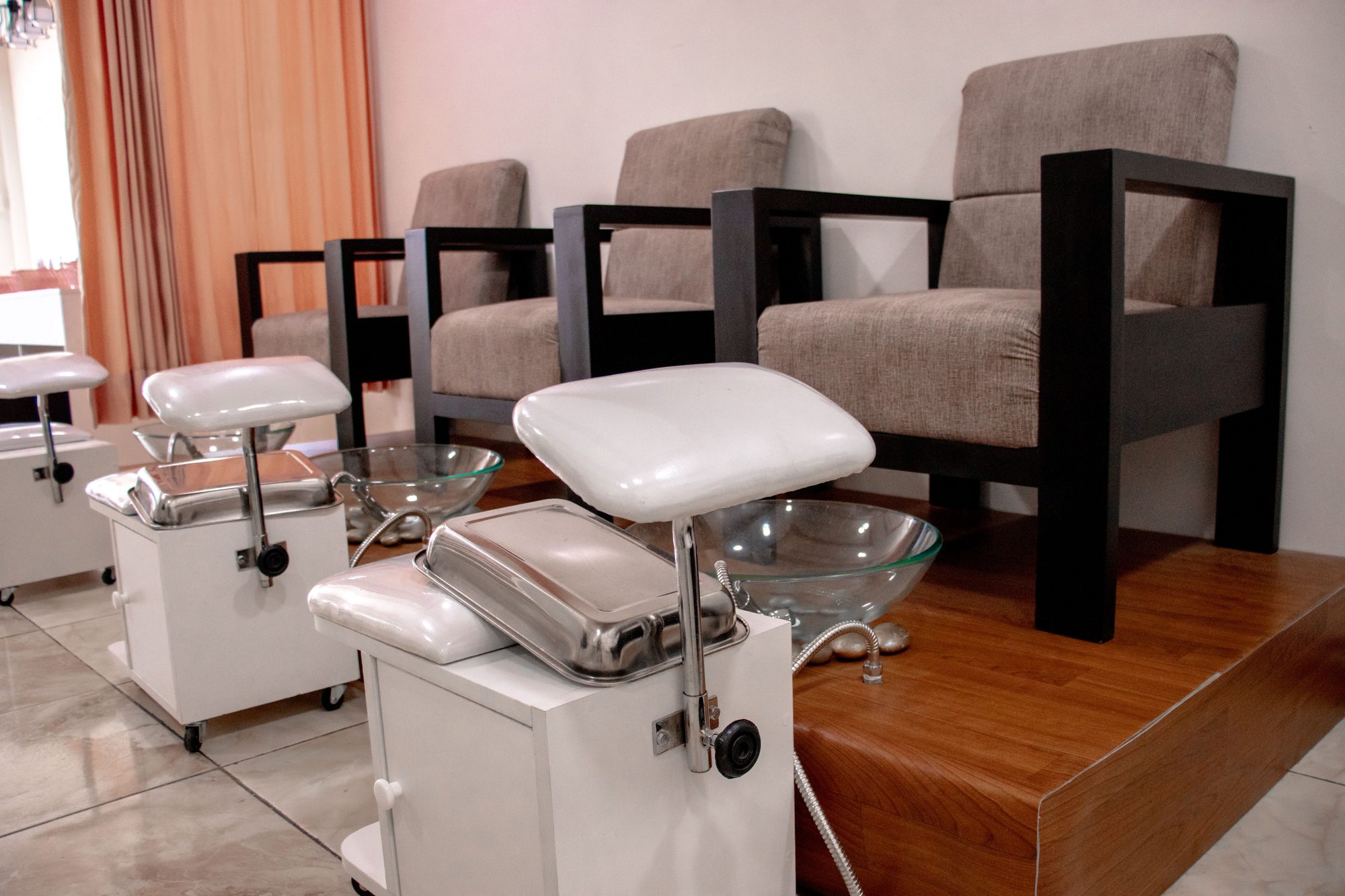 Row of upholstered pedicure chairs with glass foot-soak bowls in the bright nail bar at Verbena & Clay