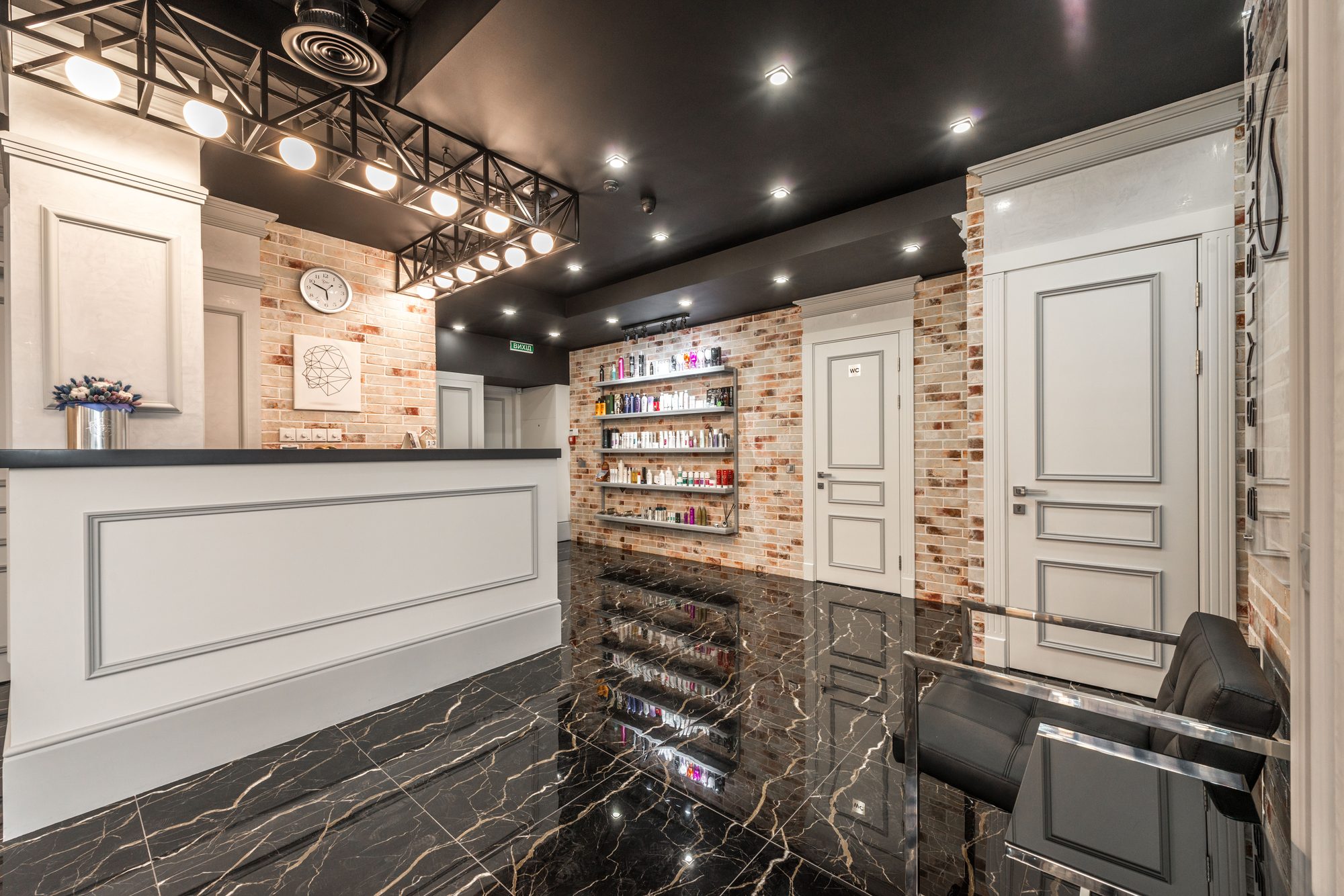 Elegant reception area at Verbena & Clay with black marble flooring and a brick accent wall lined with product shelving